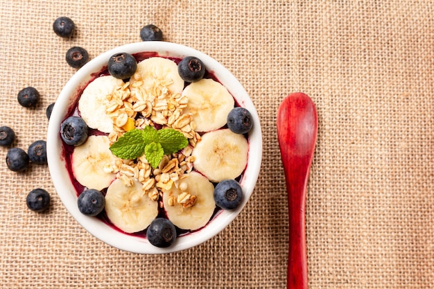 Ciotola di Acai con banana, mirtillo e cereali su tela di iuta.