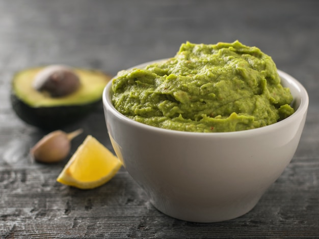 Ciotola di argilla con guacamole fresco, limone e aglio sulla tavola di legno