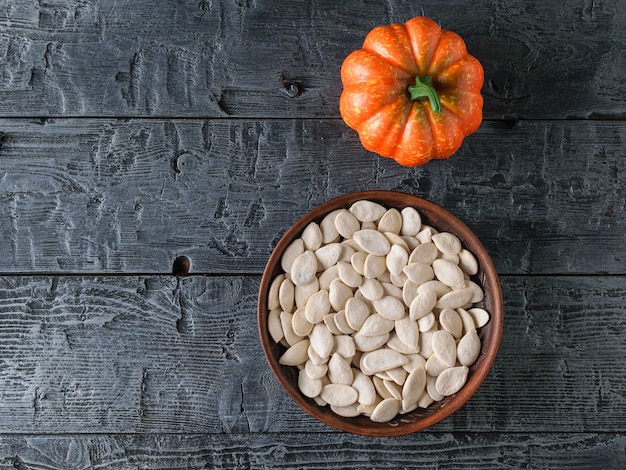 Ciotola di argilla con semi di zucca e frutta di zucca decorativa sul tavolo del villaggio