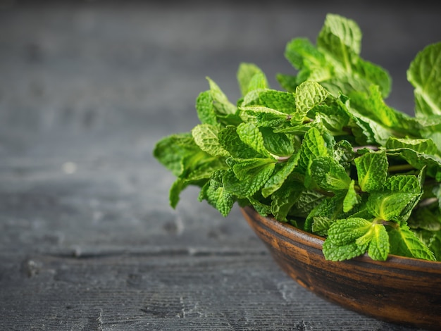 Ciotola di argilla con un mazzo di menta fresca sul tavolo di legno nero. Il concetto di alimentazione sana.