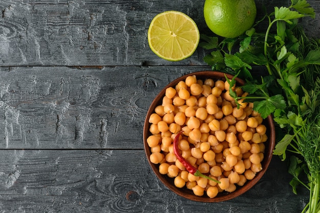 Ciotola di argilla riempita con ceci bolliti su un tavolo di legno nero con prezzemolo e lime. Cucina vegetariana a base di legumi. La vista dall'alto. Lay piatto.