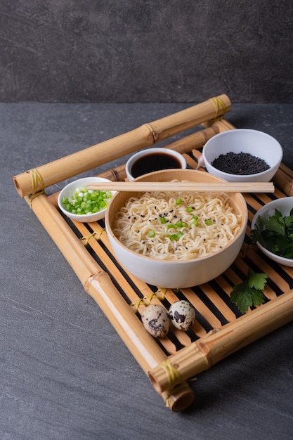 Ciotola di bambù bianco con pasta all'uovo e piatti con ingredienti su un vassoio di bambù su uno sfondo di ardesia di marmo scuro