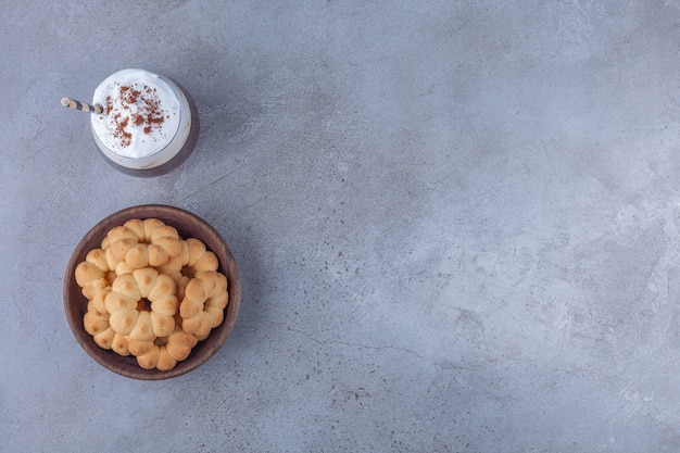 Ciotola di biscotti dolci con un bicchiere di caffè su sfondo marmo.