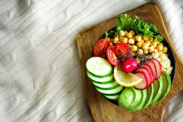 Ciotola di Buddha con avocado, quinoa, cetriolo, ravanello, insalata, limone, pomodorini, ceci, semi di chia su tessuto