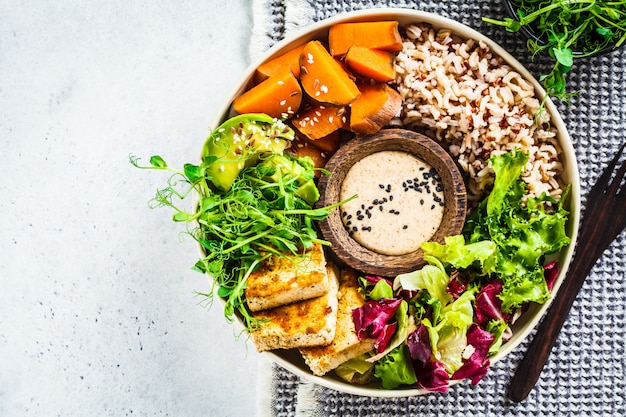 Ciotola di Buddha con salsa di tofu, avocado, riso, piantine, patate dolci e tahini.