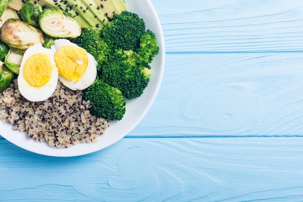 Ciotola di Buddha con uova di quinoa, avocado, cavoli di Bruxelles e broccoli, insalata vegana su sfondo di legno