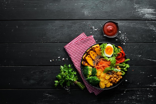 Ciotola di Buddha zucca broccoli uovo pomodori carote paprika in un piatto nero su sfondo nero Vista dall'alto Spazio libero per il testo