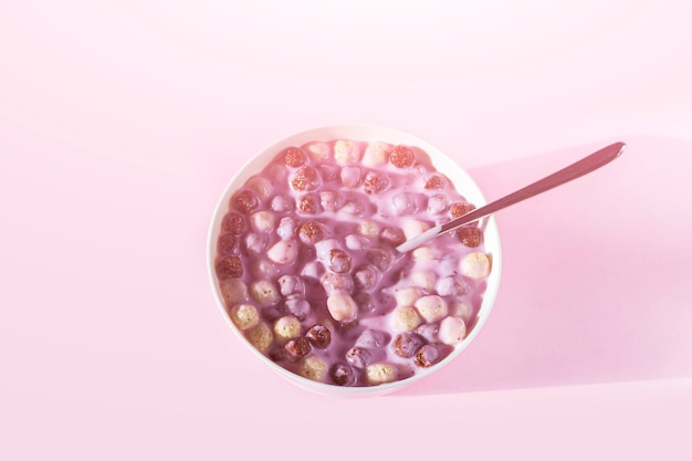 Ciotola di colazione al cioccolato e vaniglia con palline di cereali, latte o yogurt isolati su sfondo rosa. Palline di mais croccanti e sane