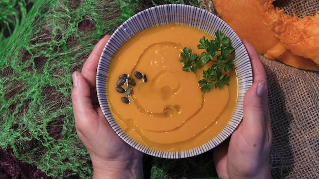 Ciotola di crema pasticcera calda della zucca di autunno che è tenuta da una persona su un fondo rustico verde e marrone