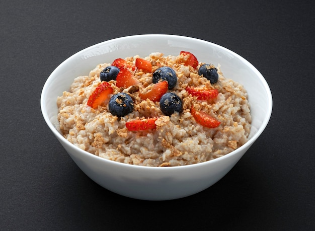 Ciotola di farina d'avena con frutti di bosco su sfondo nero