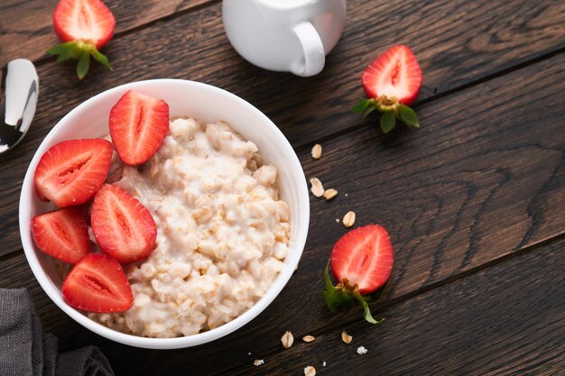 Ciotola di farina d'avena con porridge di farina d'avena con fragola, mandorla e latte su vecchio sfondo di tavolo in legno scuro Vista dall'alto in stile piatto Ingredienti naturali Colazione calda e sana e cibo dietetico