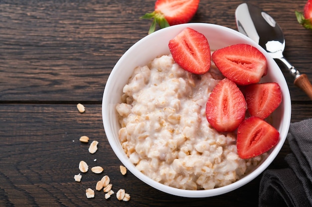 Ciotola di farina d'avena con porridge di farina d'avena con fragola, mandorla e latte su vecchio sfondo di tavolo in legno scuro Vista dall'alto in stile piatto Ingredienti naturali Colazione calda e sana e cibo dietetico