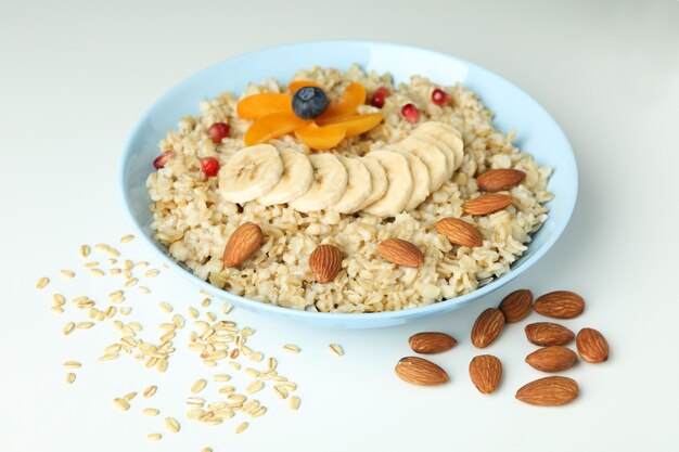 Ciotola di farina d'avena e ingredienti su sfondo bianco