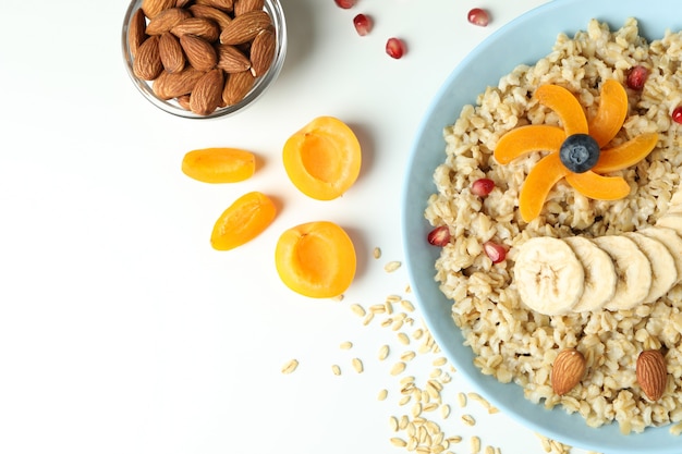 Ciotola di farina d'avena e ingredienti su sfondo bianco