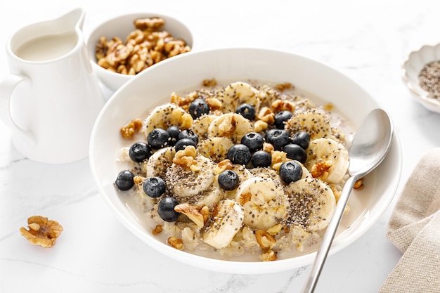 Ciotola di farina d'avena Porridge di avena con banana, mirtillo, noce, semi di chia e latte d'avena per una colazione sana Alimenti dietetici sani