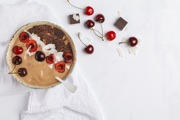 Ciotola di frullato al cioccolato - ciliegia con cocco e banane su bianco, vista dall'alto. Concetto di cibo vegano sano. Stile di vita vegano crudo.