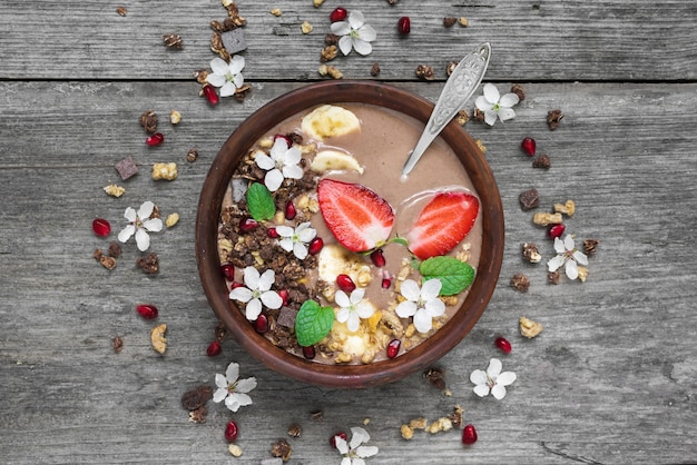 Ciotola di frullato di cioccolato e banana con muesli al cioccolato, fragole e semi di melograno con un cucchiaio