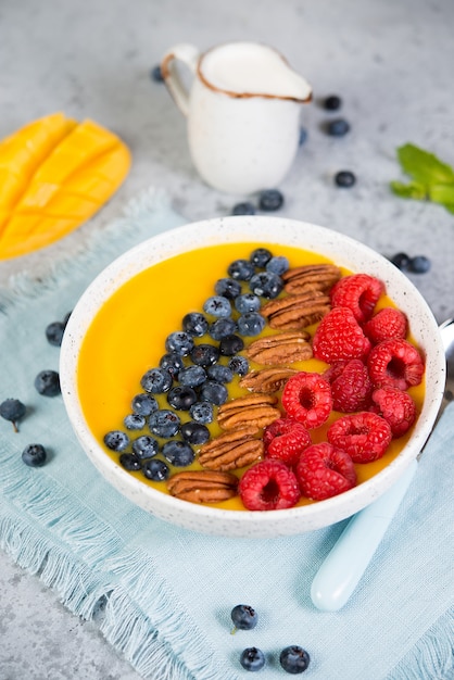 Ciotola di frullato di mango e arancia con frutti di bosco freschi e noci.