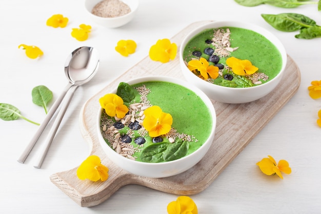 Ciotola di frullato di spinaci verdi con mirtillo, semi di chia e fiori di pansé commestibili