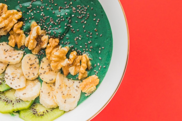 Ciotola di frullato di Spirulina con semi di banana, noci, kiwi e chia su rosso