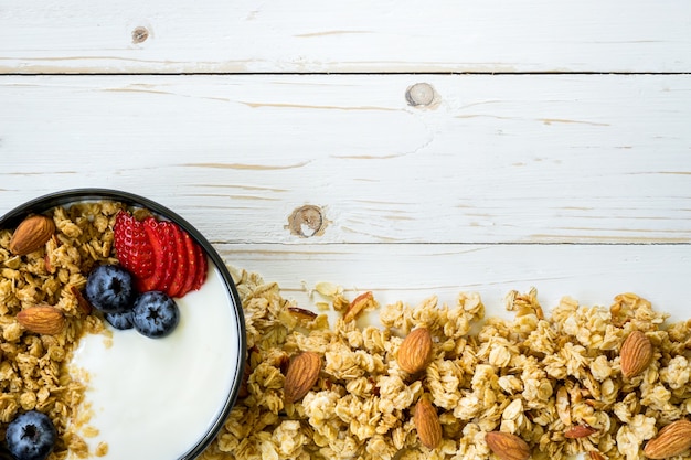 ciotola di granola con yogurt, bacche fresche, fragola sul tavolo di legno con spazio.