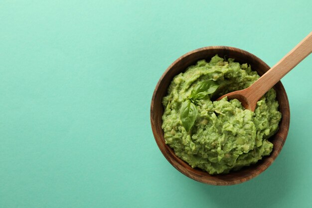 Ciotola di guacamole con cucchiaio su sfondo di menta, spazio per il testo