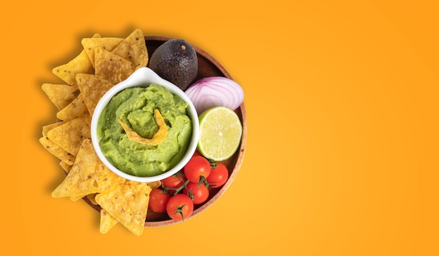 Ciotola di guacamole con nachos e ingredienti su sfondo arancione con spazio per la copia