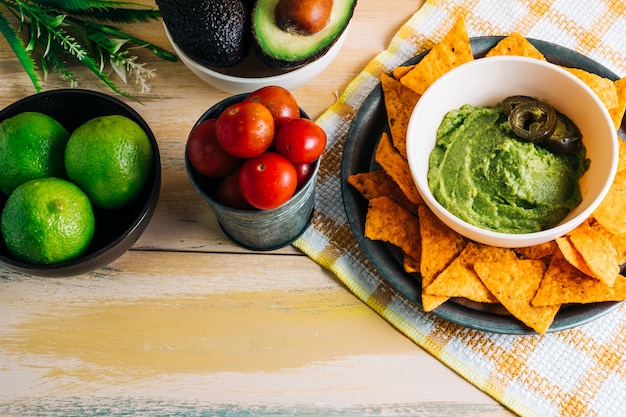 Ciotola di guacamole con nachos sul tavolo di legno d'epoca con ingredienti freschi intorno ad esso. Copia spazio. Cibo vegano