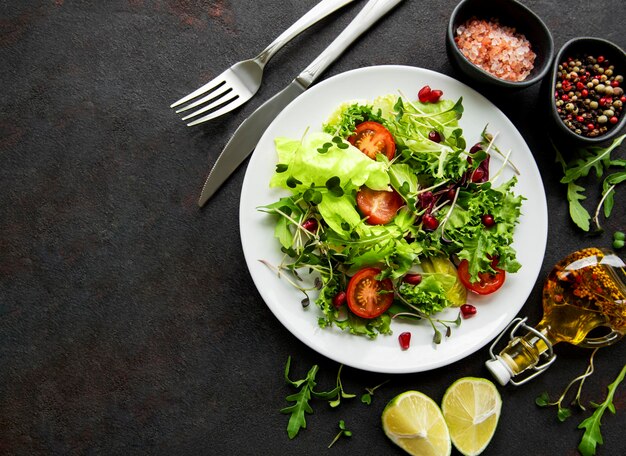 Ciotola di insalata verde fresco con pomodori e microgreen su uno sfondo di cemento nero.