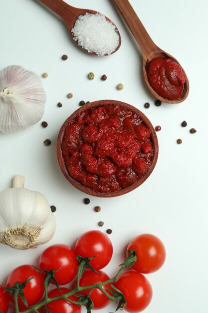 Ciotola di legno con concentrato di pomodoro e ingredienti su sfondo bianco