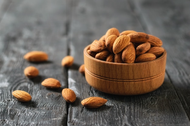 Ciotola di legno con mandorle sulla tavola di legno nera. Cibo vegetariano.