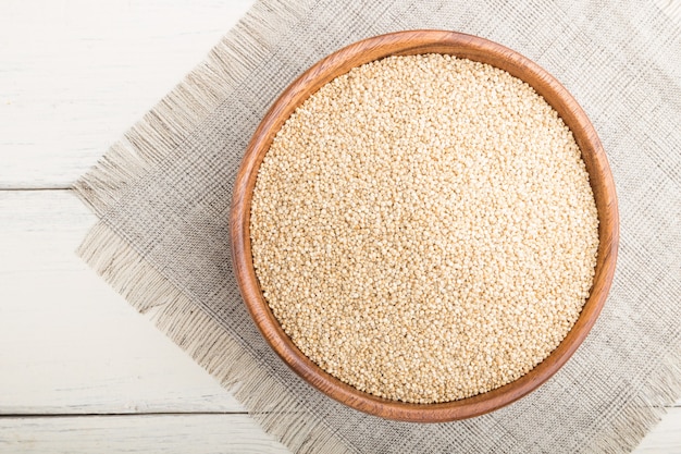 Ciotola di legno con semi di quinoa bianca cruda su una superficie di legno bianca e tessuto di lino