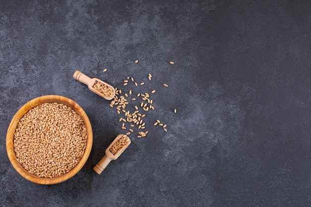 Ciotola di legno di chicchi di grano su sfondo nero