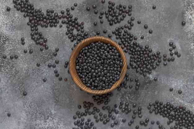 Ciotola di legno di fagioli di lenticchie nere secche su tavolo grigio vista dall'alto fonte proteica per la dieta vegetariana