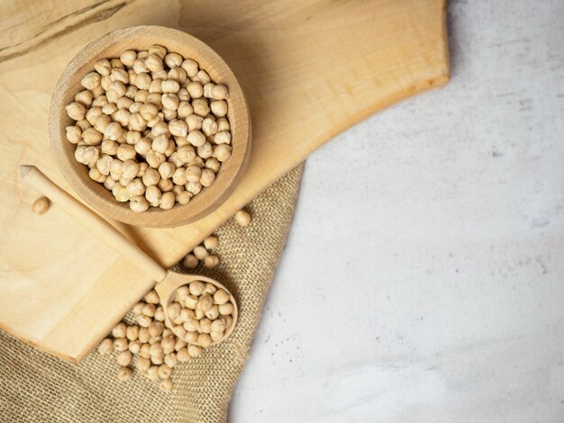 Ciotola di legno e cucchiaio di legno pieno di ceci su uno sfondo di cemento chiaro. avvicinamento