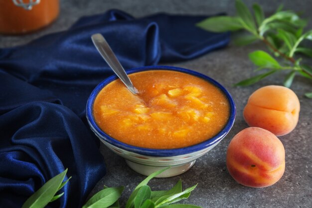 Ciotola di marmellata di albicocche con frutta e foglie sul tavolo grigio