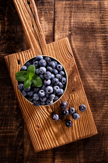 Ciotola di mirtilli freschi sulla tavola di legno rustica. Mirtilli di alimenti biologici e foglia di menta per uno stile di vita sano.