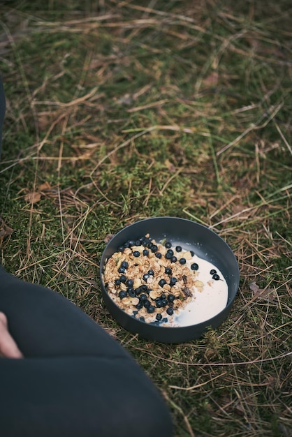 Ciotola di muesli fatto in casa con yogurt e frutti di bosco freschi durante l'escursione all'aperto Muesli allo yogurt e frutti di bosco in una ciotola di ceramica su sfondo di erba