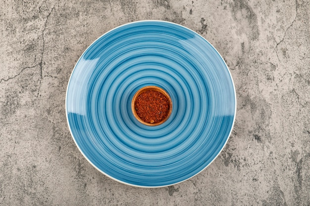 Ciotola di peperoncino rosso in polvere posto sulla piastra blu.