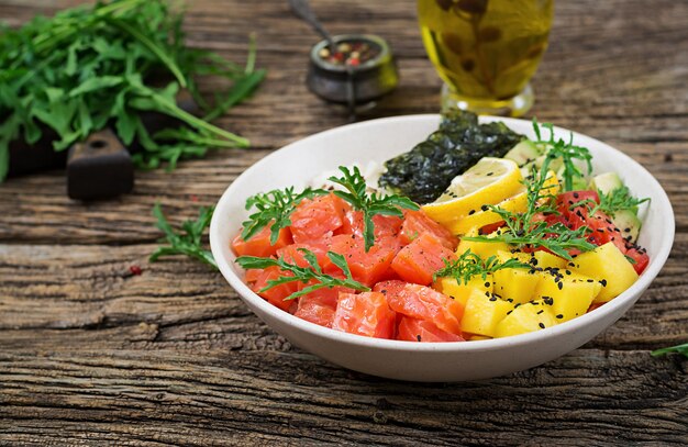 Ciotola di poke di pesce salmone hawaiano con riso, avocado, mango, pomodoro, semi di sesamo e alghe.