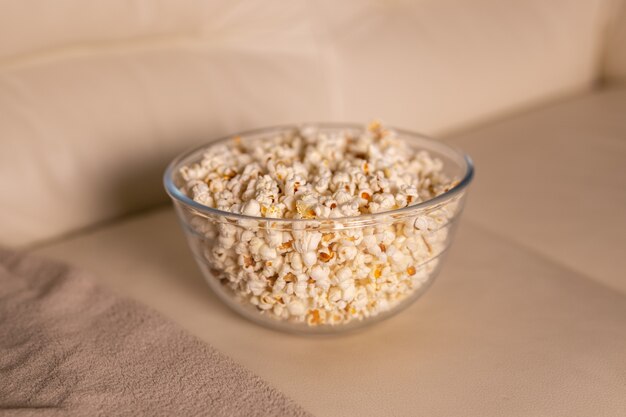 Ciotola di popcorn per guardare un film su un divano beige, snack e un concetto malsano di cibo spazzatura