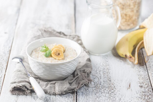 Ciotola di porridge di farina d'avena con banana su tavola rustica in legno bianco, colazione sana, cibo dietetico.