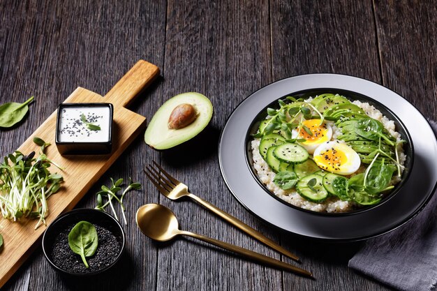 Ciotola di quinoa con uovo con microgreens di girasole, cetriolo, avocado, spinaci in una ciotola nera su un tavolo di legno scuro, cucina turca