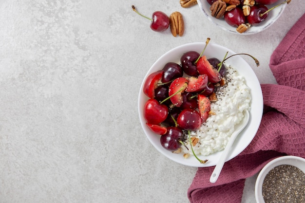 Ciotola di ricotta con bacche fresche di ciliegia, prugne, noci pecan, semi di chia e latte su una superficie grigio chiaro