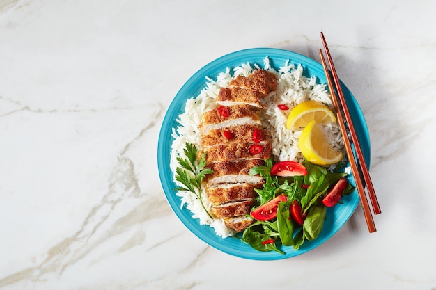 Ciotola di riso condita con cotoletta di petto di pollo impanata fritta servita con insalata di pomodori e spinaci, vista orizzontale dall'alto