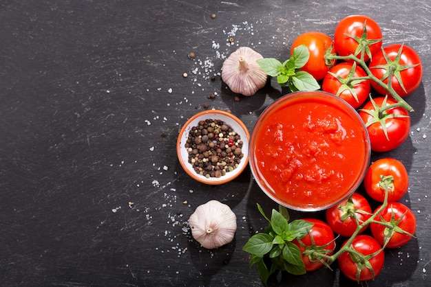 Ciotola di salsa di pomodoro con verdure fresche sul tavolo scuro, vista dall'alto