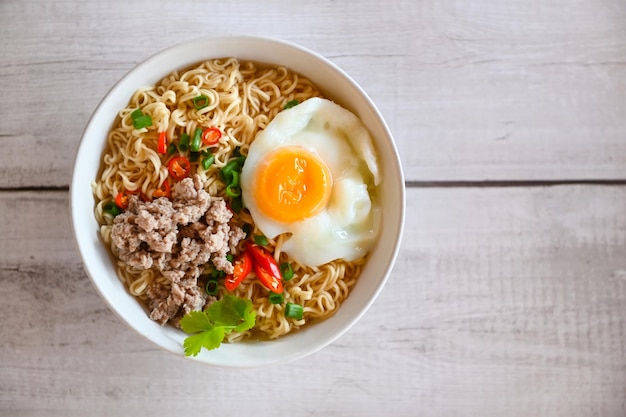 Ciotola di tagliatelle con uovo sodo carne di maiale tritata verdura cipollotto limone lime lattuga sedano e peperoncino sul tavolo cibo spaghetti istantanei cucina gustoso mangiare con ciotola zuppa di noodle