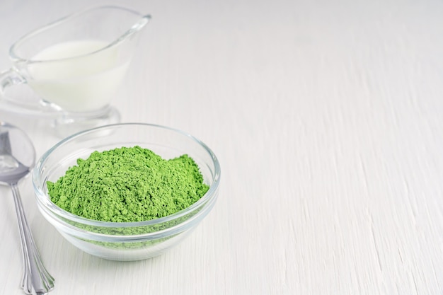 Ciotola di tè verde matcha disintossicante biologico lascia polvere macinata con latte e cucchiaio sul tavolo bianco