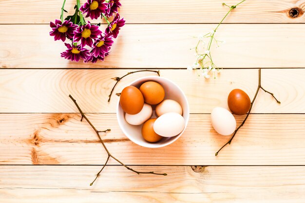 Ciotola di uova in ceramica, fondo in legno piatto, preparazione di Pasqua, prodotti agricoli, uovo di gallina, decorazione di una casa, rami di un albero con gemme, primavera, bellissimi fiori rosso brillante, crisantemi