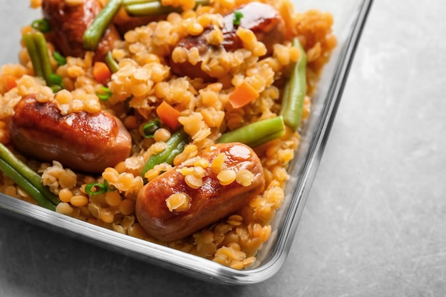 Ciotola di vetro con gustose salsicce di porridge di lenticchie e verdure sul primo piano del tavolo da cucina